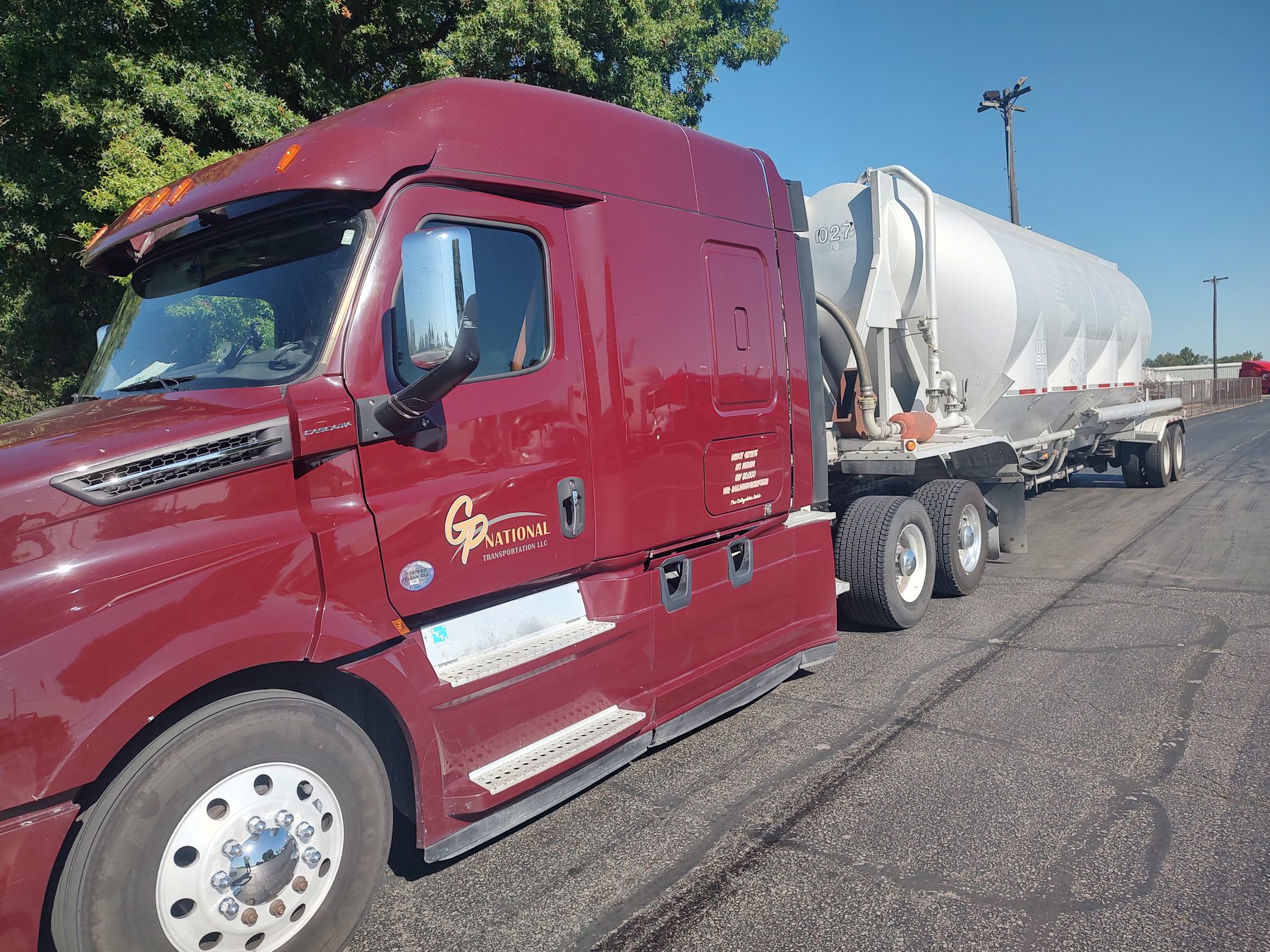 Close-up of the GP National logo on the door of a maroon Freightliner Cascadia, with the white pneumatic trailer behind