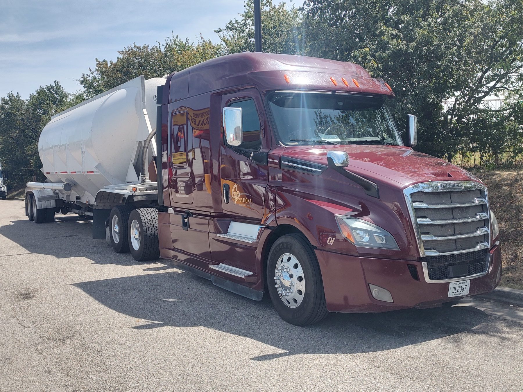GP National maroon Freightliner Cascadia tractor pulling a white pneumatic bulk trailer